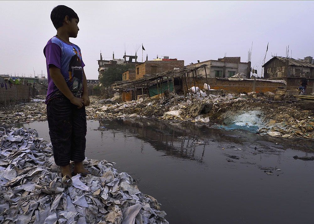 A boy standing on a mound of discarded leather scraps by a tannery canal in Hazaribagh, Dhaka.